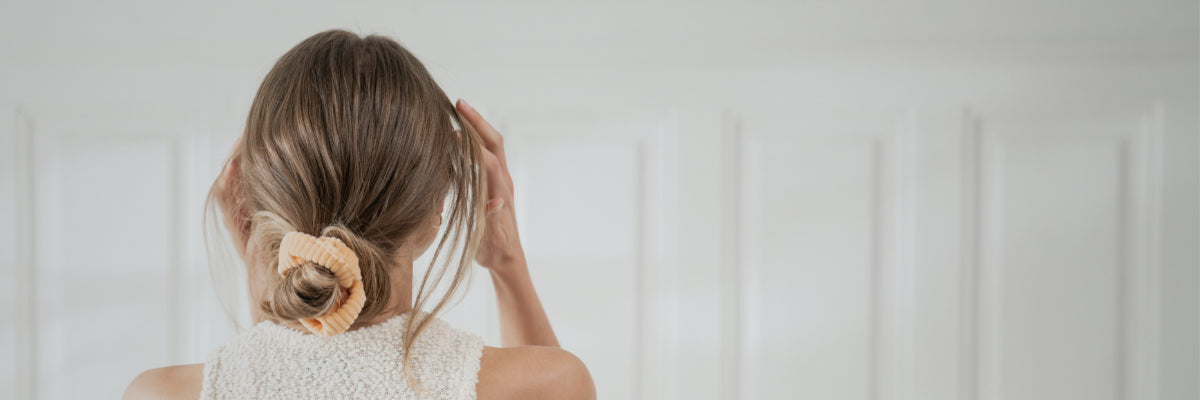 Blonde Frau von hinten mit einem orangenen Baumwoll-Scrunchie