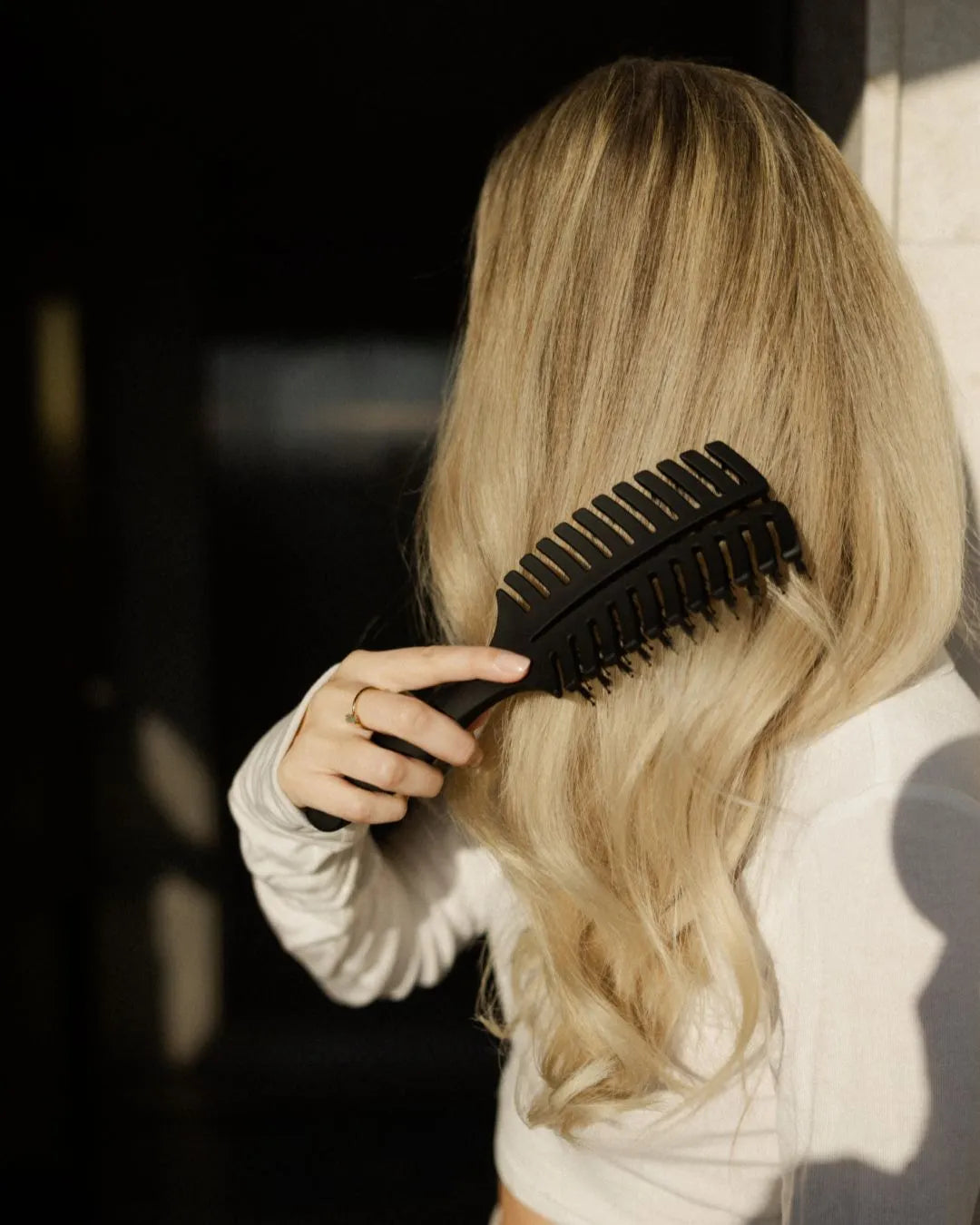 Frau mit blonden Haaren kämmt sich mit einer schwarzen Haarbürste von feschi die Haare durch