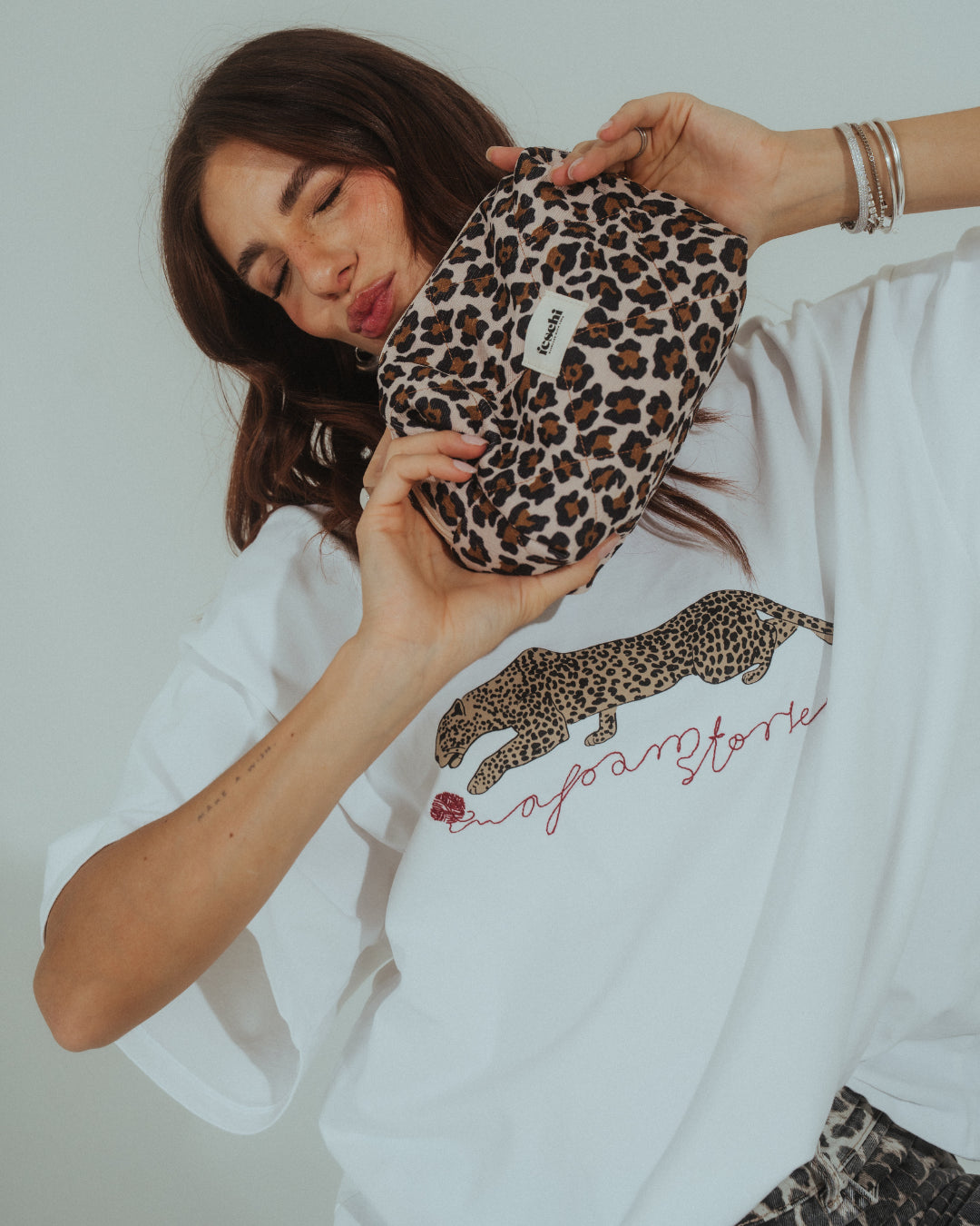 Frau hält eine Kosmetiktasche von feschi mit Leomuster in der Hand und macht einen Kussmund