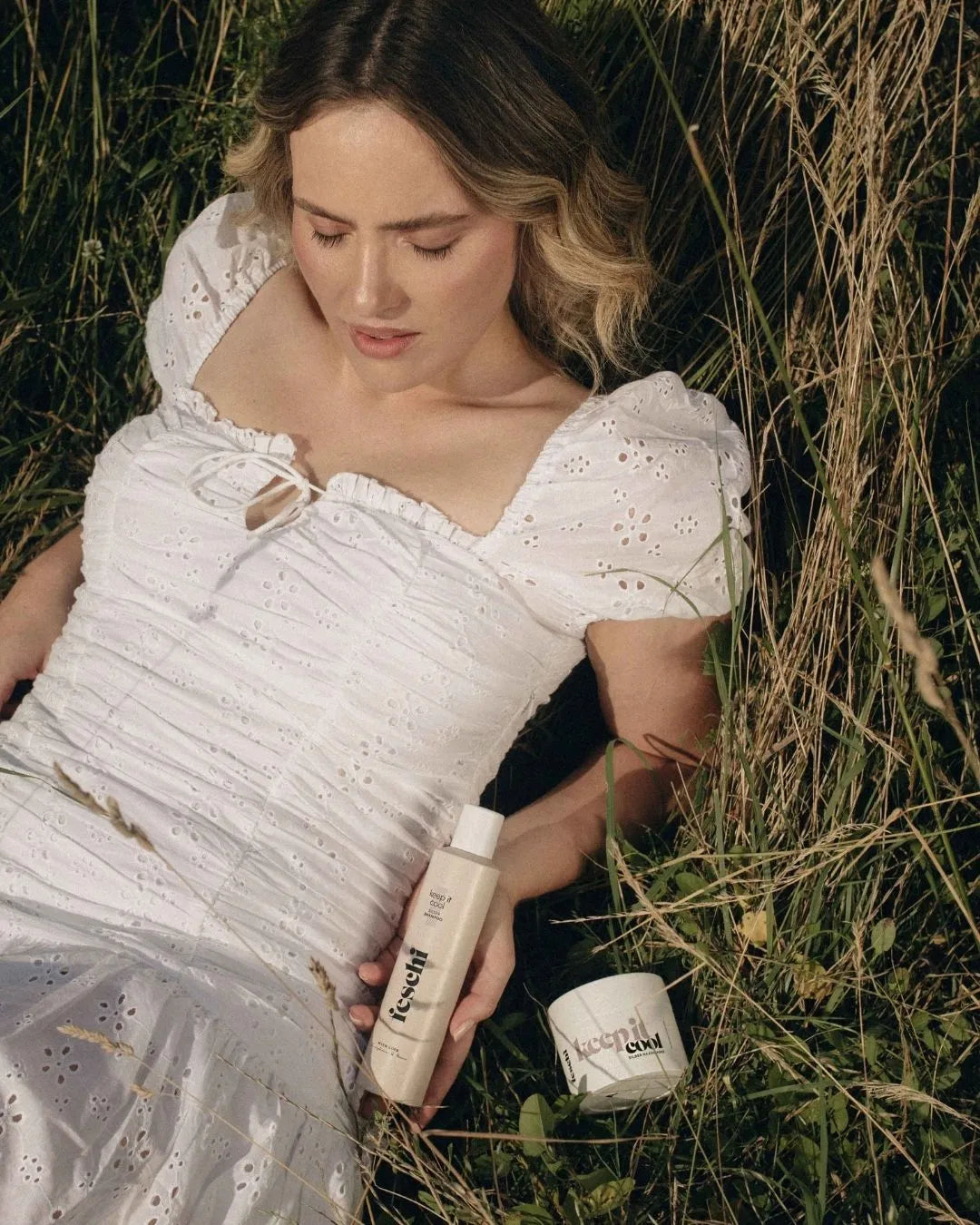 Blonde Frau liegt in Gras und neben ihr liegen die Silberprodukte von feschi Haircare