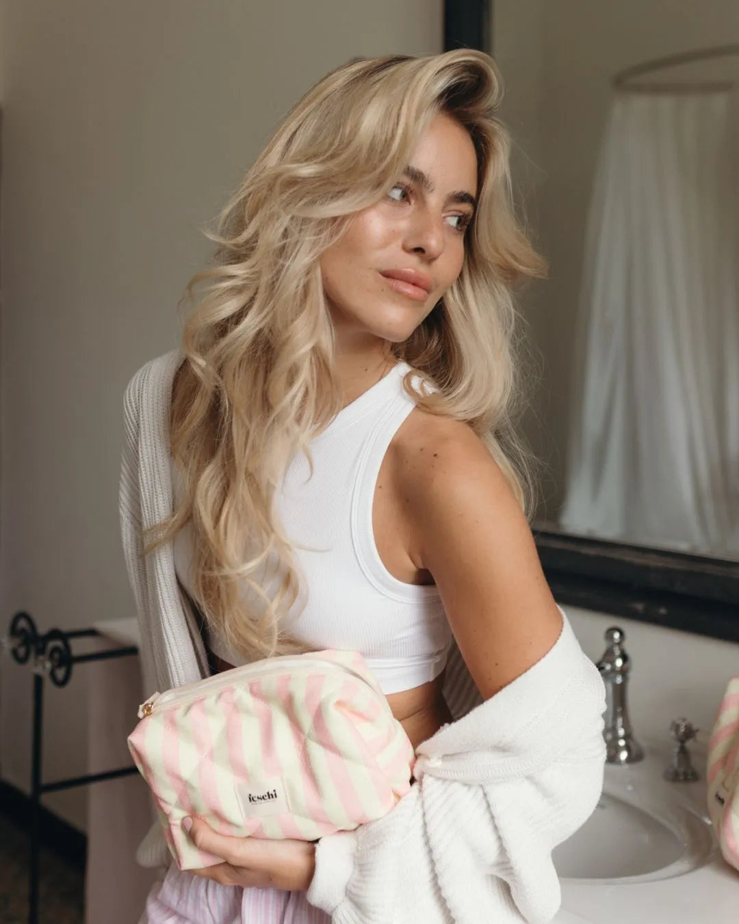 Frau steht in Badezimmer und hält feschi Schminktasche in der Hand