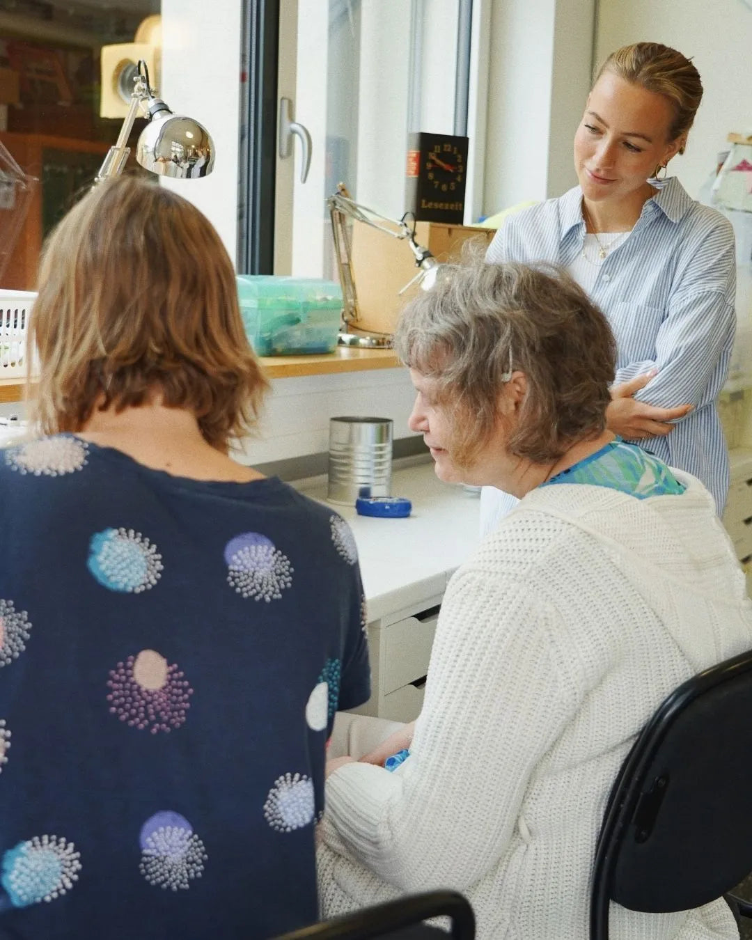 Drei Frauen, die vor einem Schreibtisch sitzen/stehen
