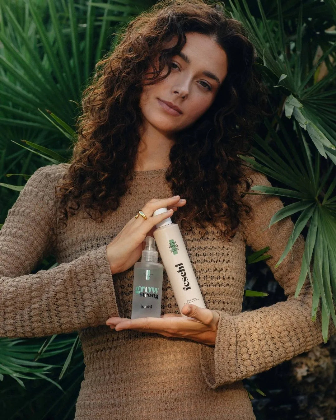 Frau mit Locken steht vor einer Palme und hÀlt die zwei feschi grow strong - Produkte in der Hand