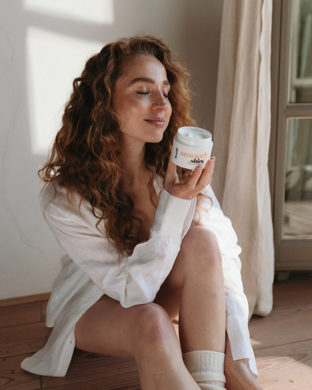 Frau sitzt am Boden und riecht an Macadamia Maske von feschi