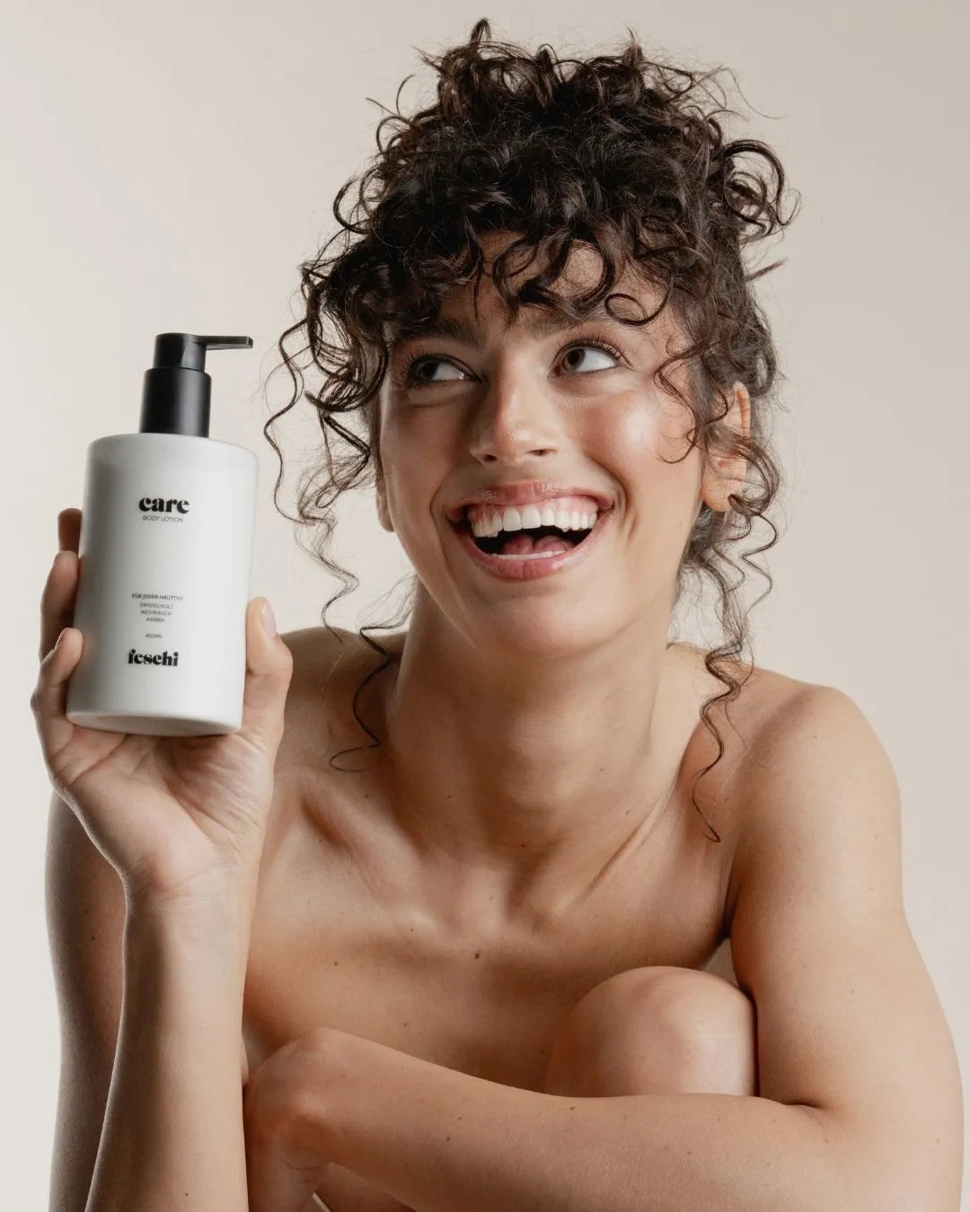 Lachende Frau hält feschi care Body Lotion in der Hand - intensive Feuchtigkeitspflege mit Sandelholz & Ambra.