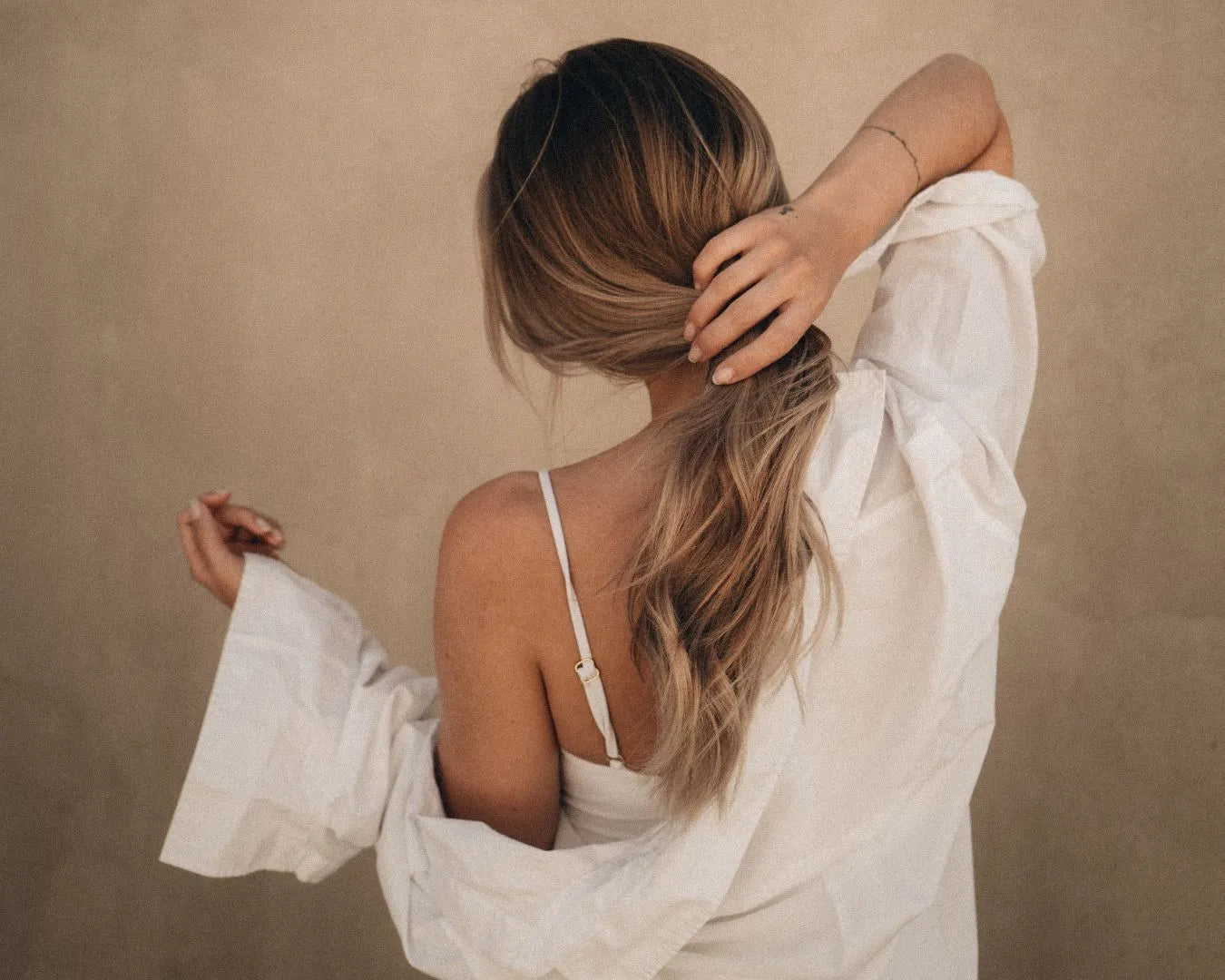 Frau vor Wand fasst sich an Haare