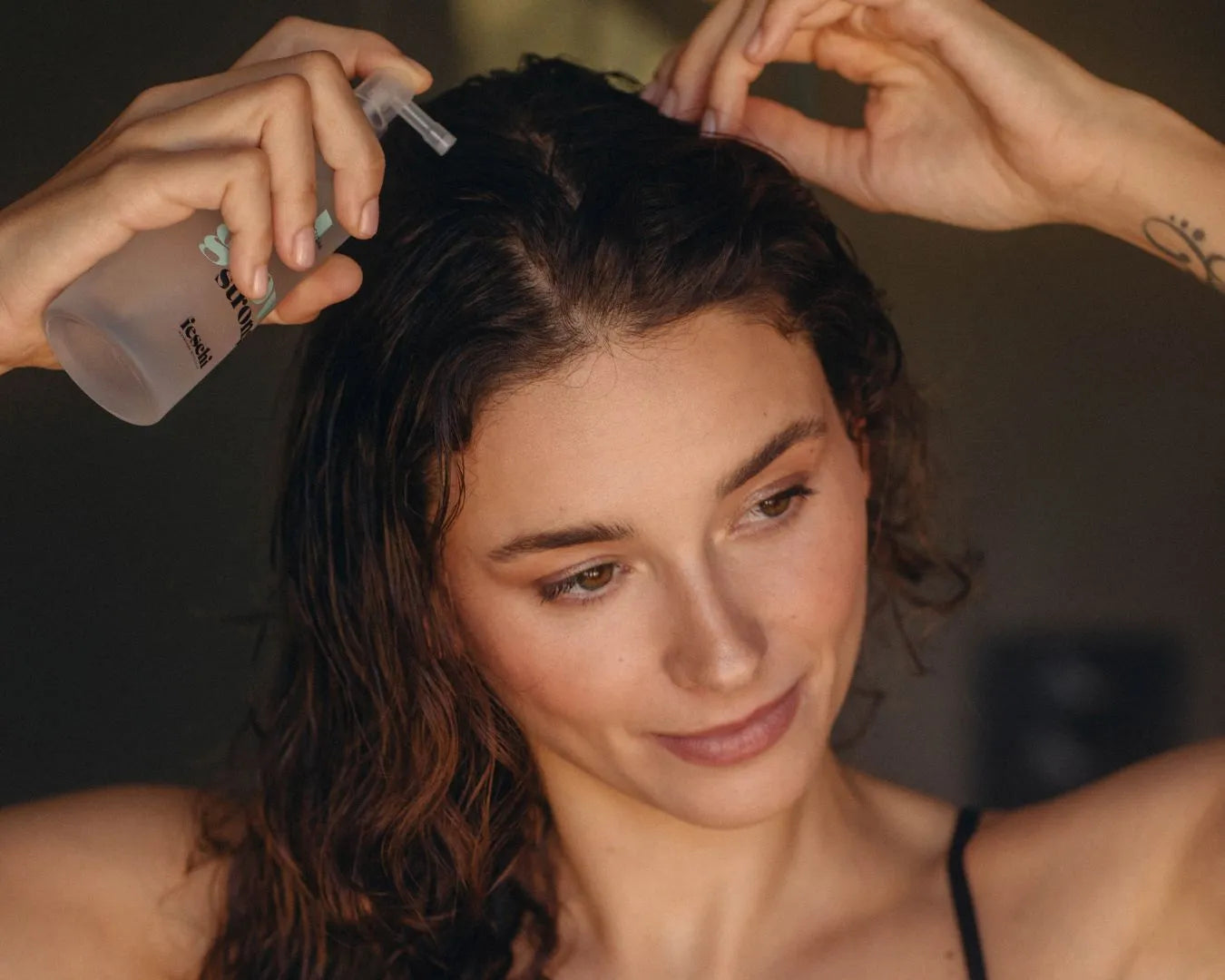 Frau wendet das grow strong tonic von feschi im handtuchtrockenen Haar an