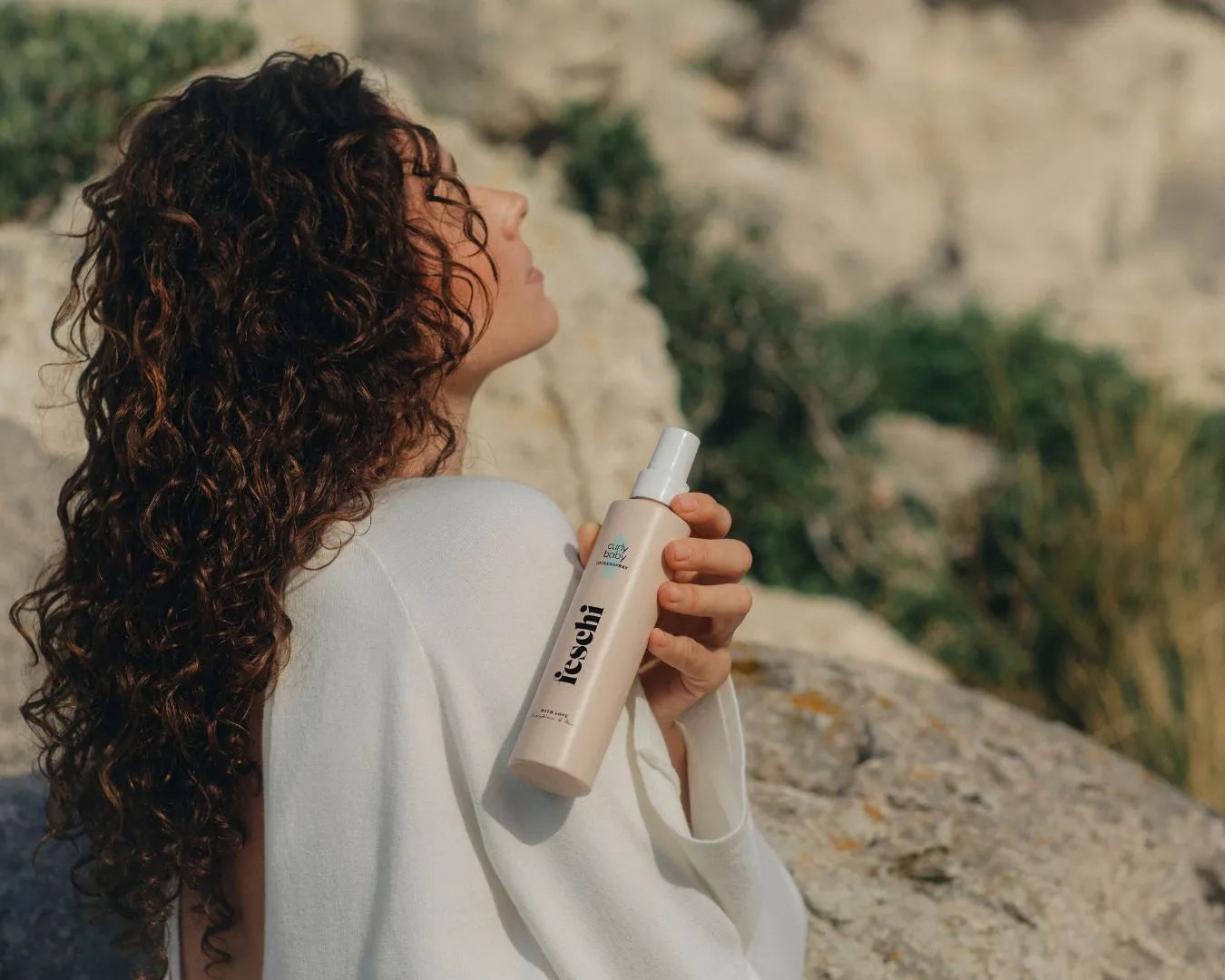 Frau die vor Steinformationen steht, lockiges Haar hat und das curly baby Lockenspray von fesch in die Kamera zeigt