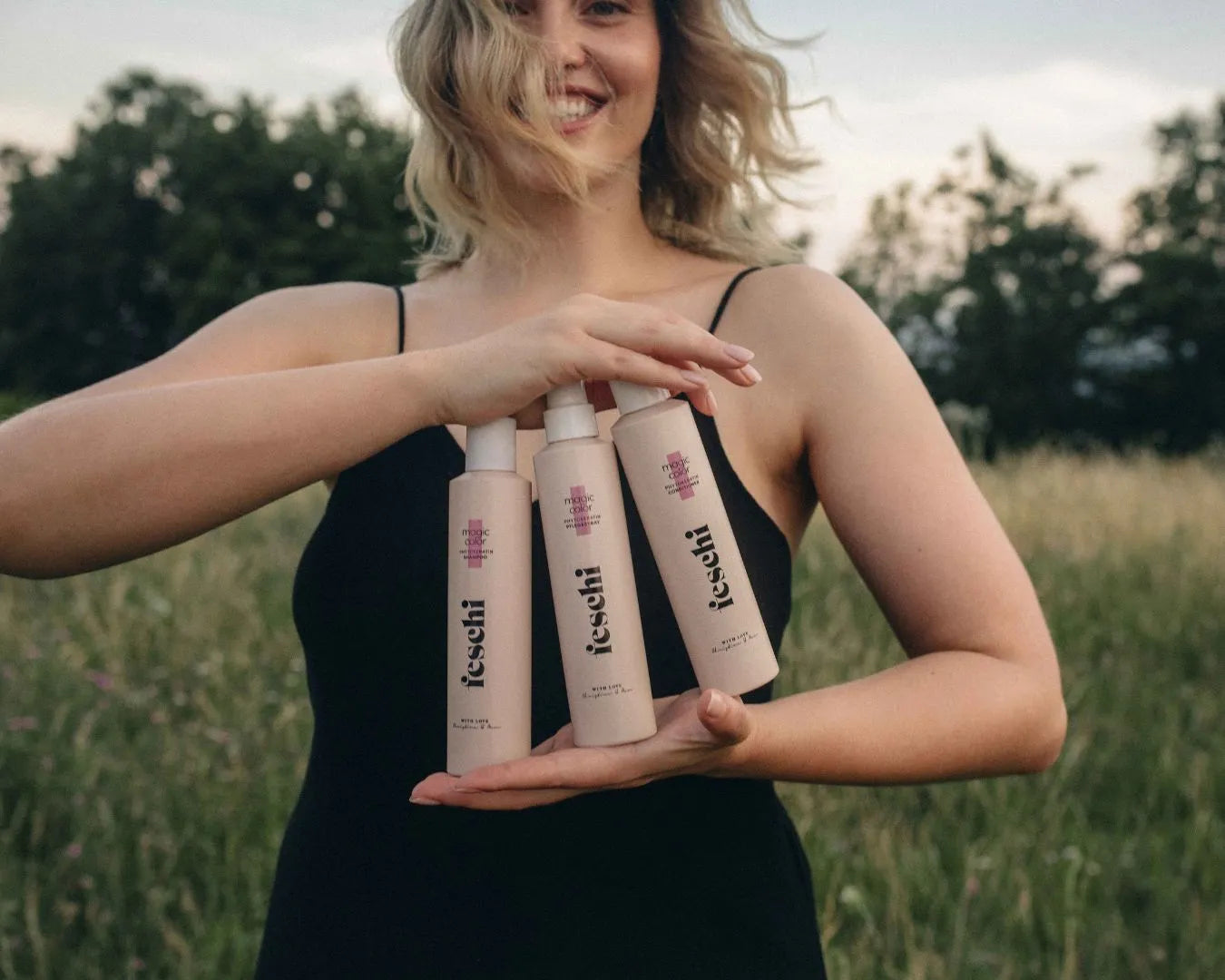 Lächelnde Frau, die in Wiese steht und drei feschi Produkte der intense care - Serie in der Hand hält