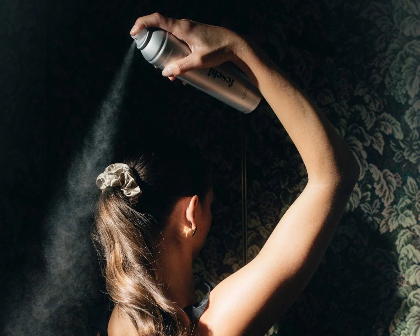 Person mit langen Haaren sprĂŒht sich Haarspray in Zopf