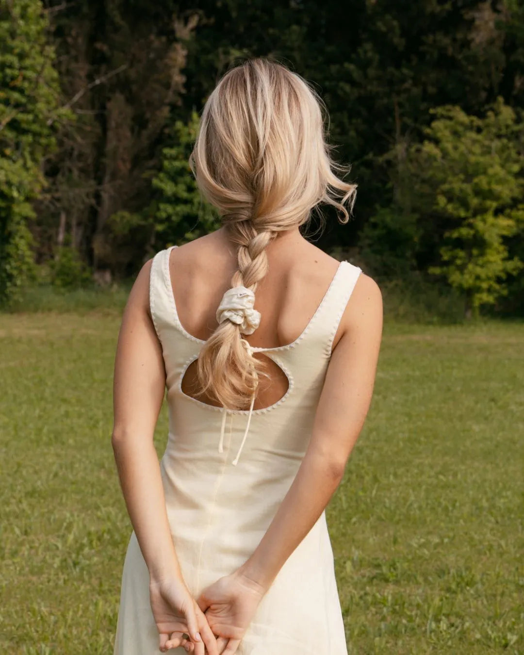 Frau von hinten mit verschrĂ€nkten Armen im RĂŒcken, trĂ€gt einen geflochtenen Zopf mit weiĂem Seiden-Scrunchie von feschi