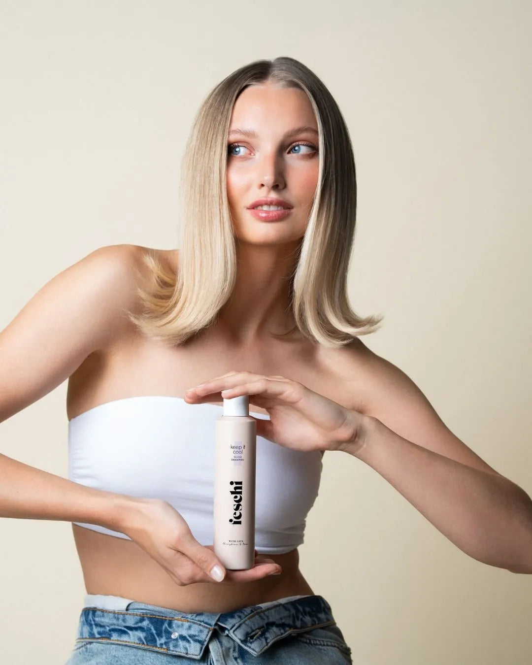 blonde Frau hält keep it cool Silber Shampoo von feschi in ihren Händen und schaut von der Kamera weg