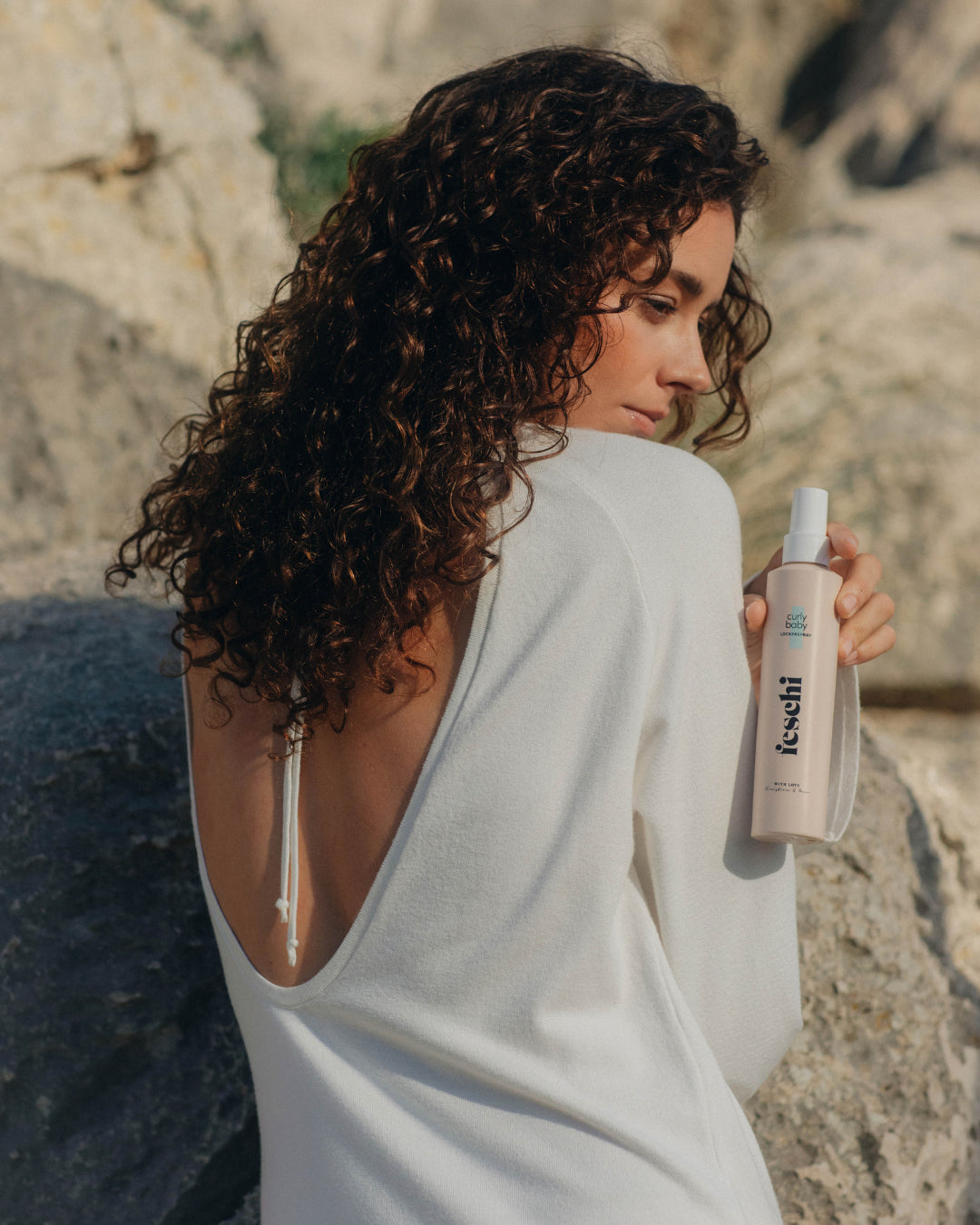 Frau mit braunen Naturlocken präsentiert den curly baby Lockenspray von feschi - maximaler Halt ohne zu verkleben, perfekt für Naturhaar oder Locken