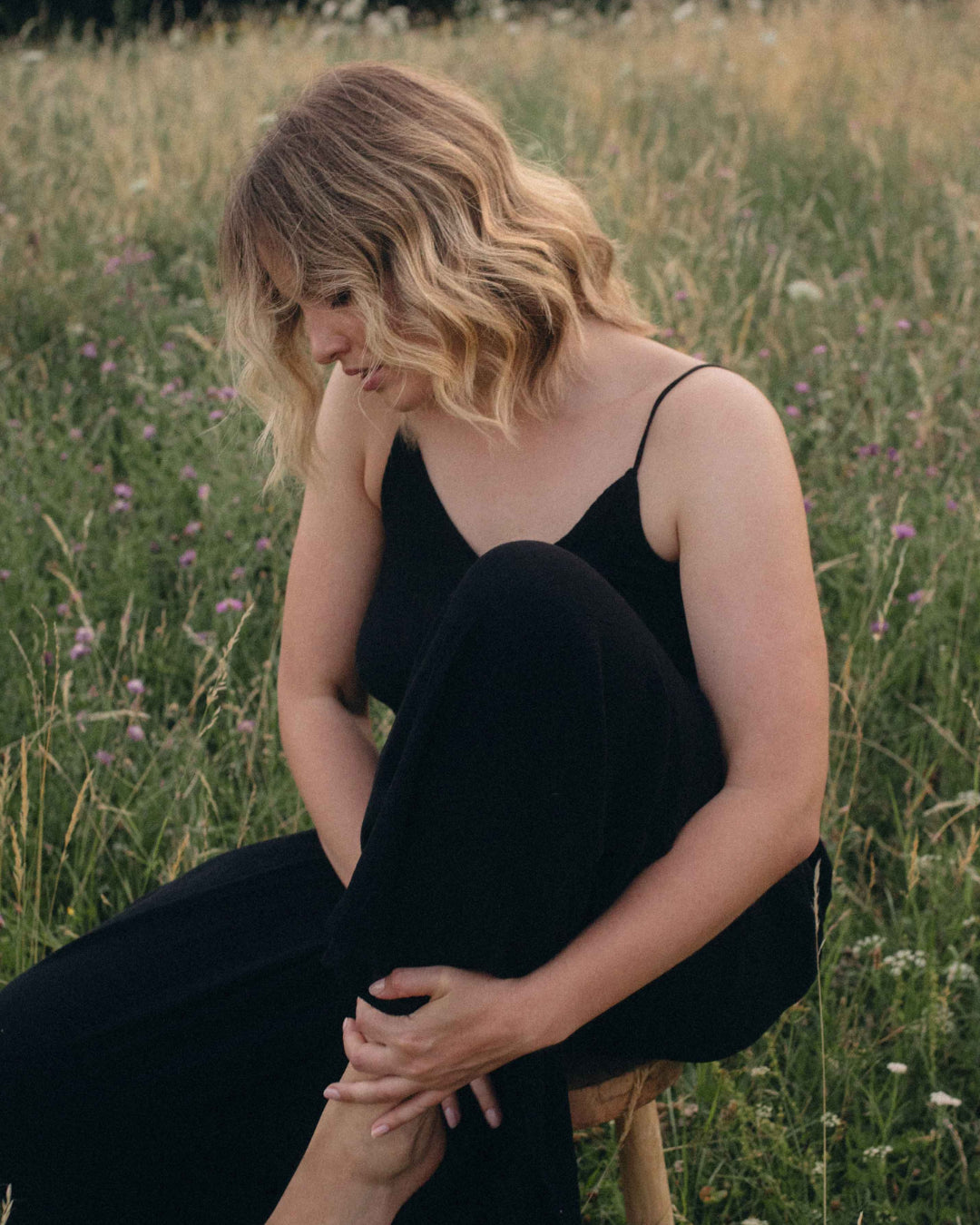 blonde Frau mit gelocktem Haar sitzt auf grünem Feld. feschi Set für strapaziertes Haar