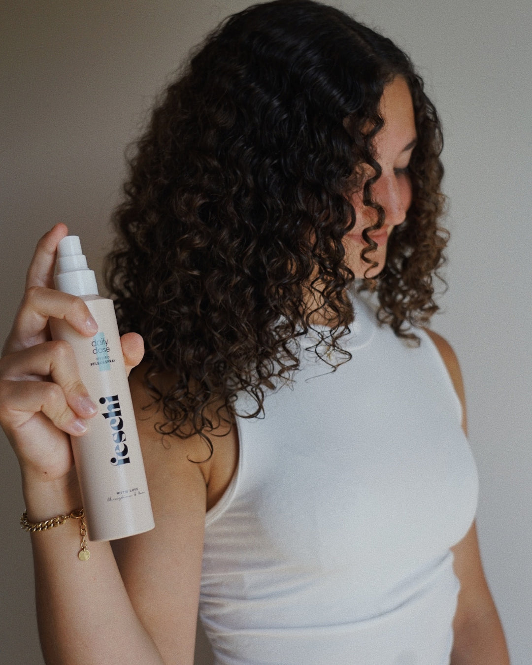 junge Frau mit lockigem Naturhaar sprüht den feschi daily dose Pflegespray ins Haar. Für Glanz & Geschmeidigkeit