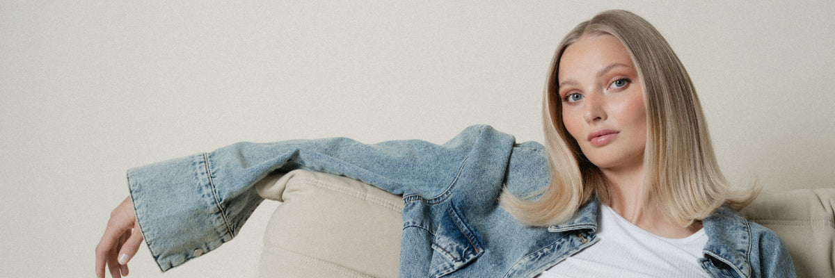 Blonde Frau sitzt mit Jeansjacke gemütlich auf einem Sofa