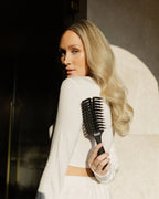 Blonde Frau blickt über Schulter und hält die feschi Hair Brush in der Hand