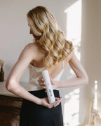 Frau mit glänzenden Haaren hält das Anti Frizz Spray von feschi hinter ihrem Rücken