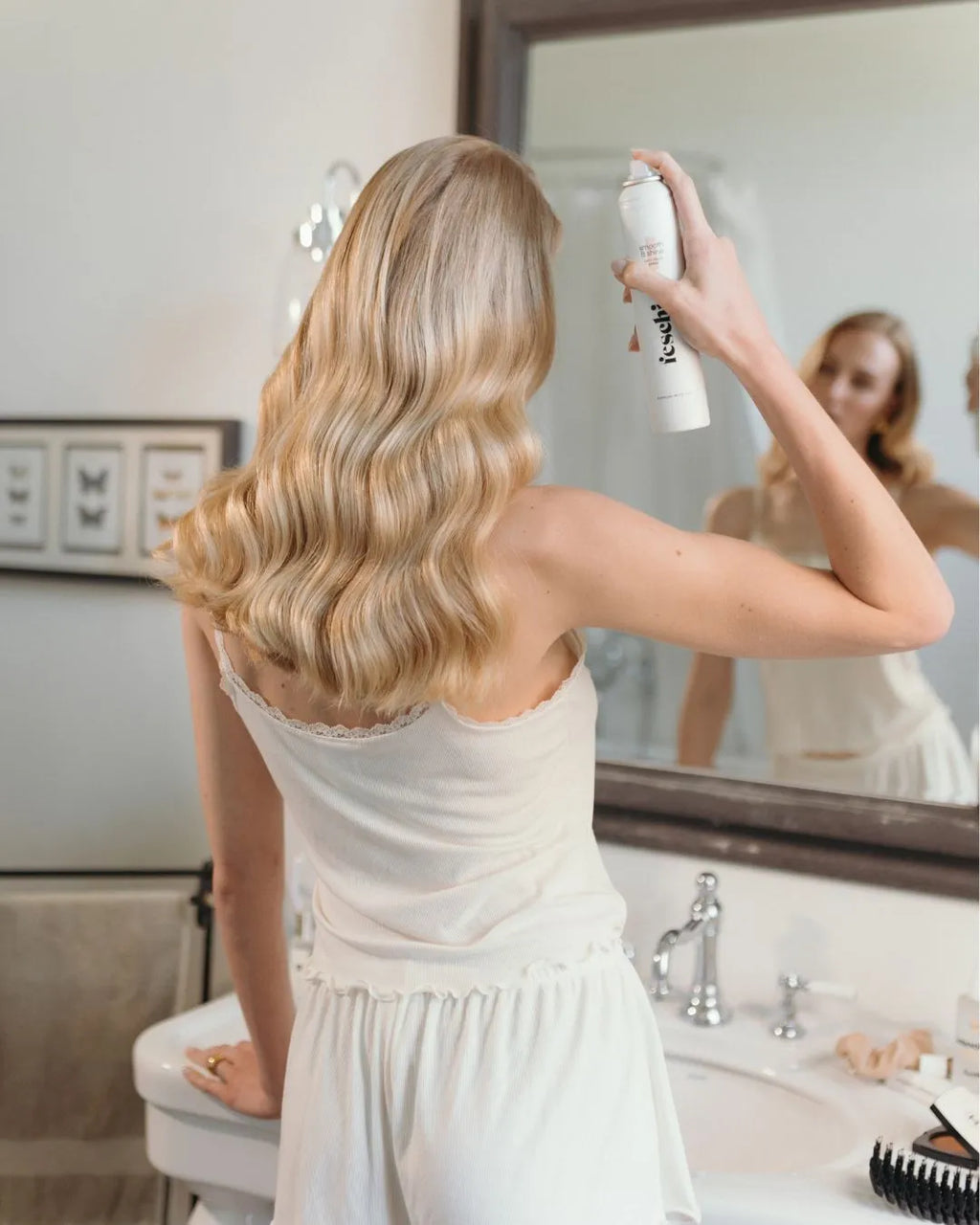 Frau steht in Badezimmer und sprüht ihre Haare mit Anti Frizz Spray von feschi an