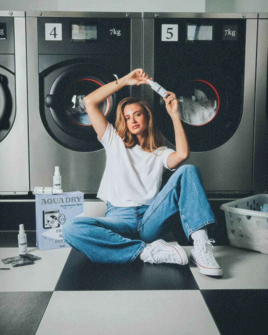 Frau sitzt am Boden vor Waschmaschinen und hält das Trockenshampoo Liquid von feschi über ihren Kopf
