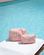 Zwei gelb-pinke Kosmetiktaschen stehen auf Sonnenliege vor Pool