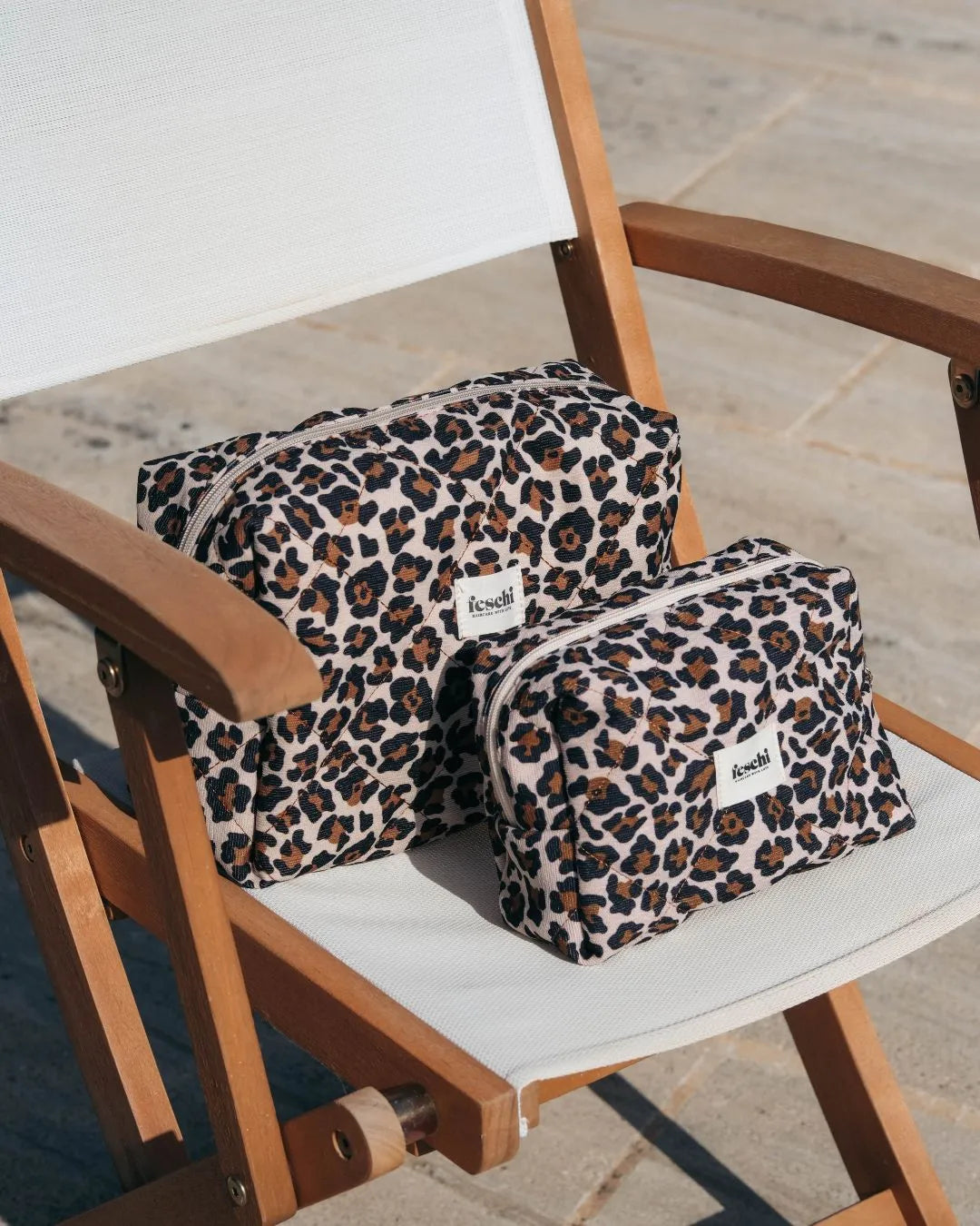 Zwei Leopard Beauty Bags von feschi in unterschiedlichen Größen stehen auf Stuhl