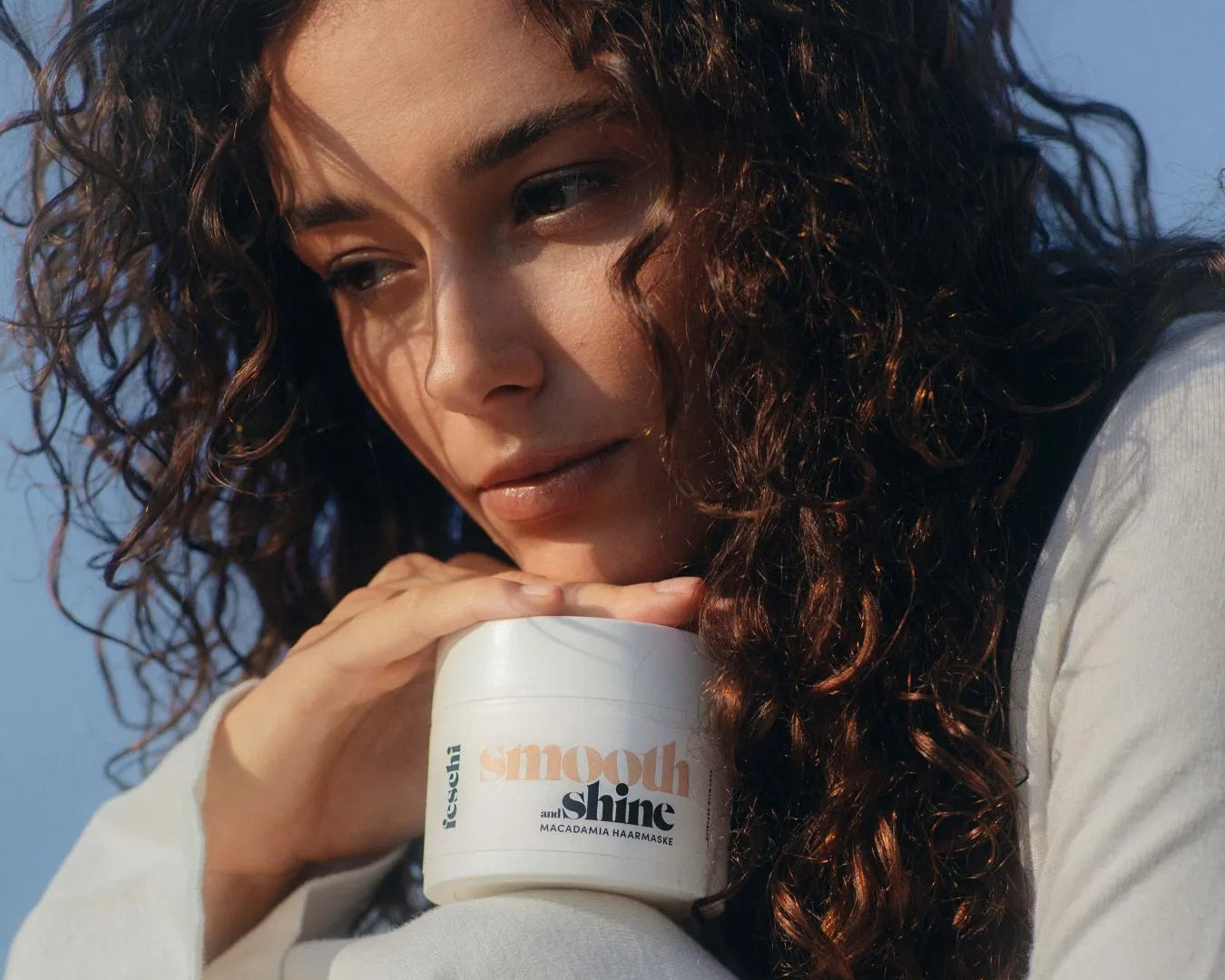 Frau mit starken Locken lehnt sich an smooth & shine Maske von feschi an 
