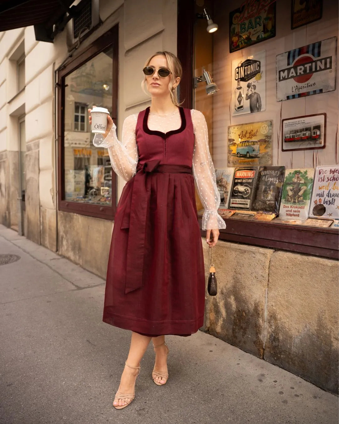 Frau im weinroten Dirndl mit Kaffeebecher in der Hand