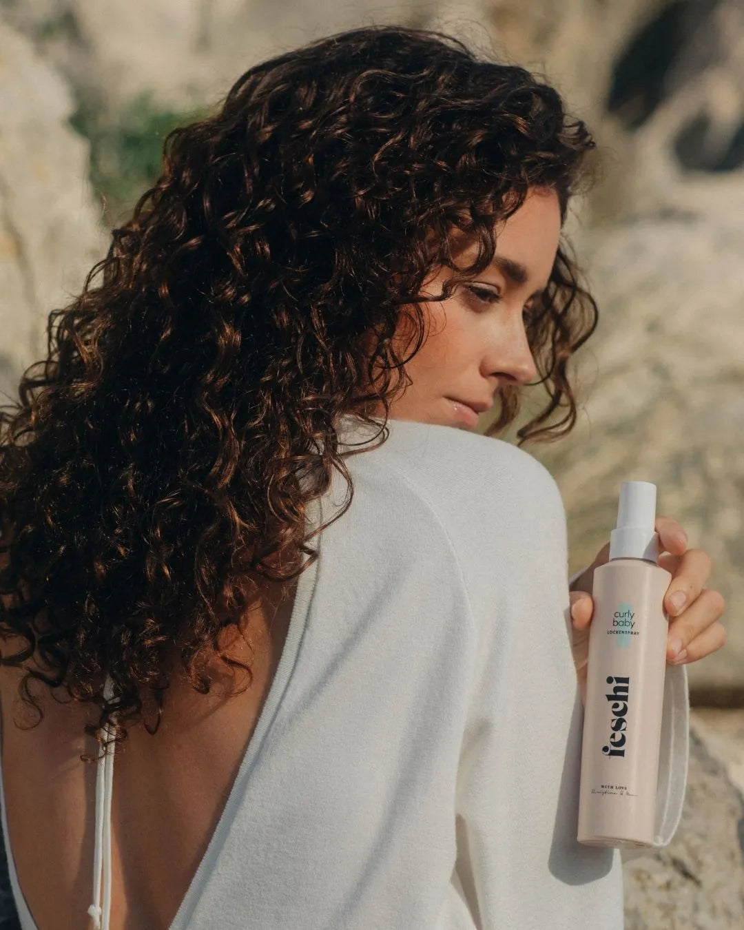 Eine Frau mit lockigem Haar hält das Lockenspray von feschi in der Hand