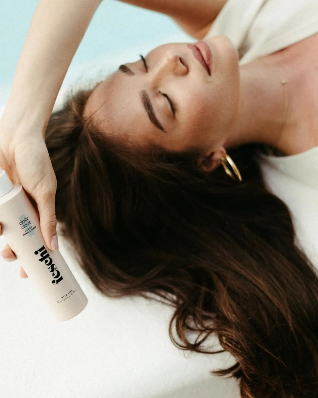 Frau mit dunklen Haaren liegt am Poolrand-Becken und hält den daily dose Conditioner von feschi in der Hand