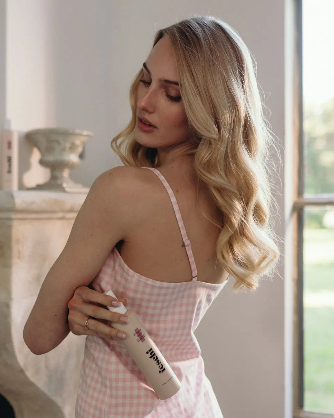 Frau mit blonden lockigen Haaren und rosa Pyjama hält das intense care - Repair Spray von feschi in der Hand