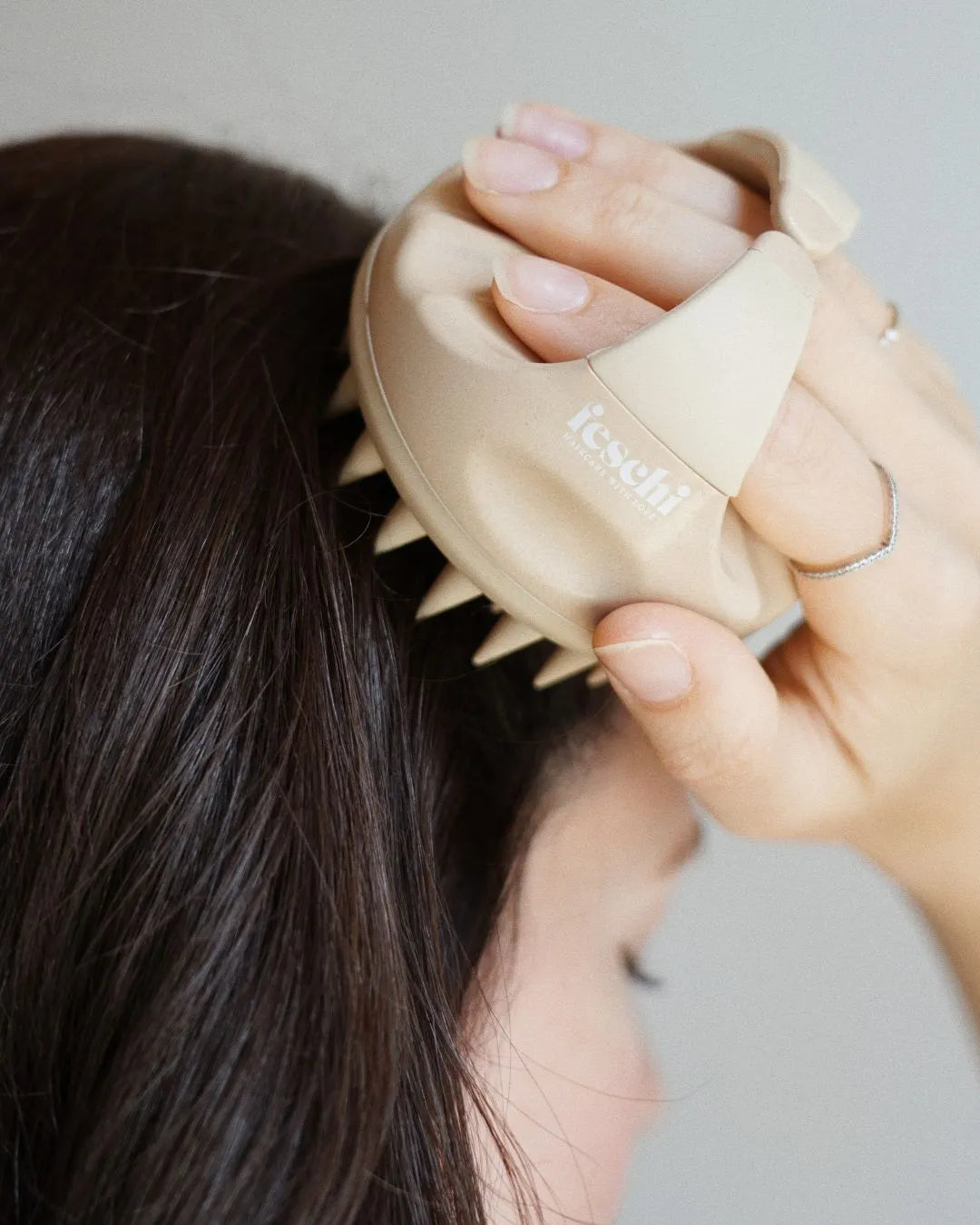 Person mit dunkelbraunen Haaren massiert sich mit der scalp brush von feschi die Kopfhaut