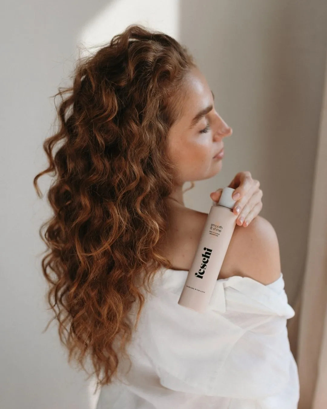 Frau mit lockigem Haar hält das smooth & shine Macadamia Shampoo von feschi in der Hand