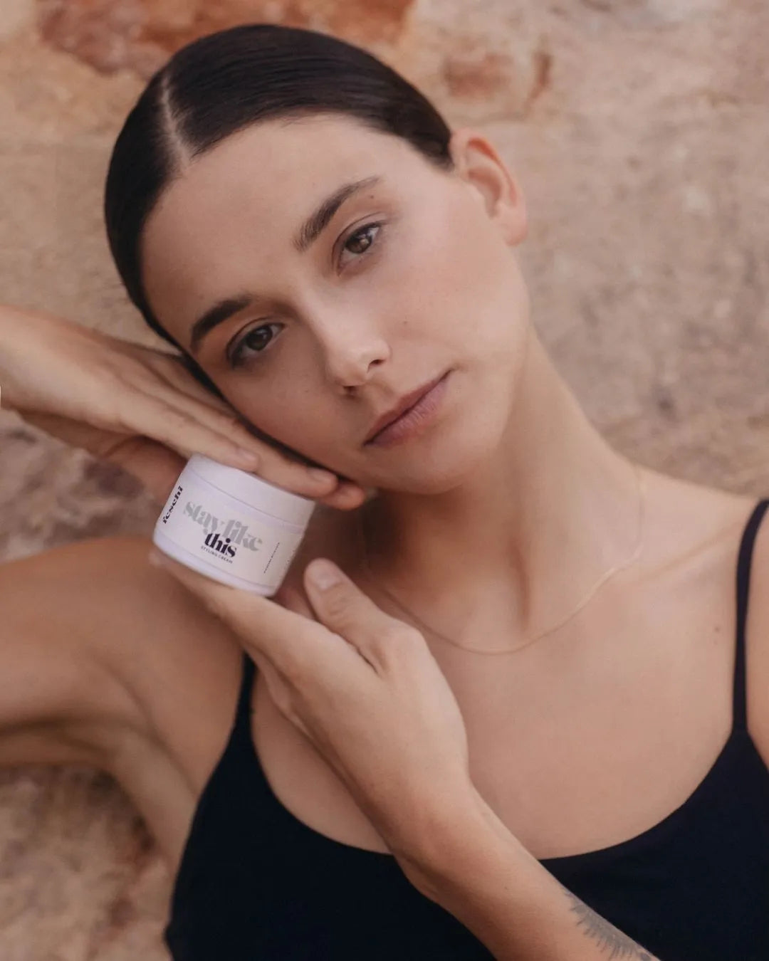 Frau mit strengem Zopf hält die Styling Cream von feschi in der Hand und blickt verträumt in die Kamera