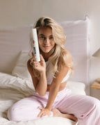 Frau mit langen blonden Haaren sitzt im Bett und hält das feschi The One and Only Trockenshampoo in der Hand