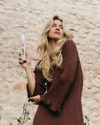 Frau steht vor einer Hauswand und hält das feschi Intense Care Repair Spray in der Hand