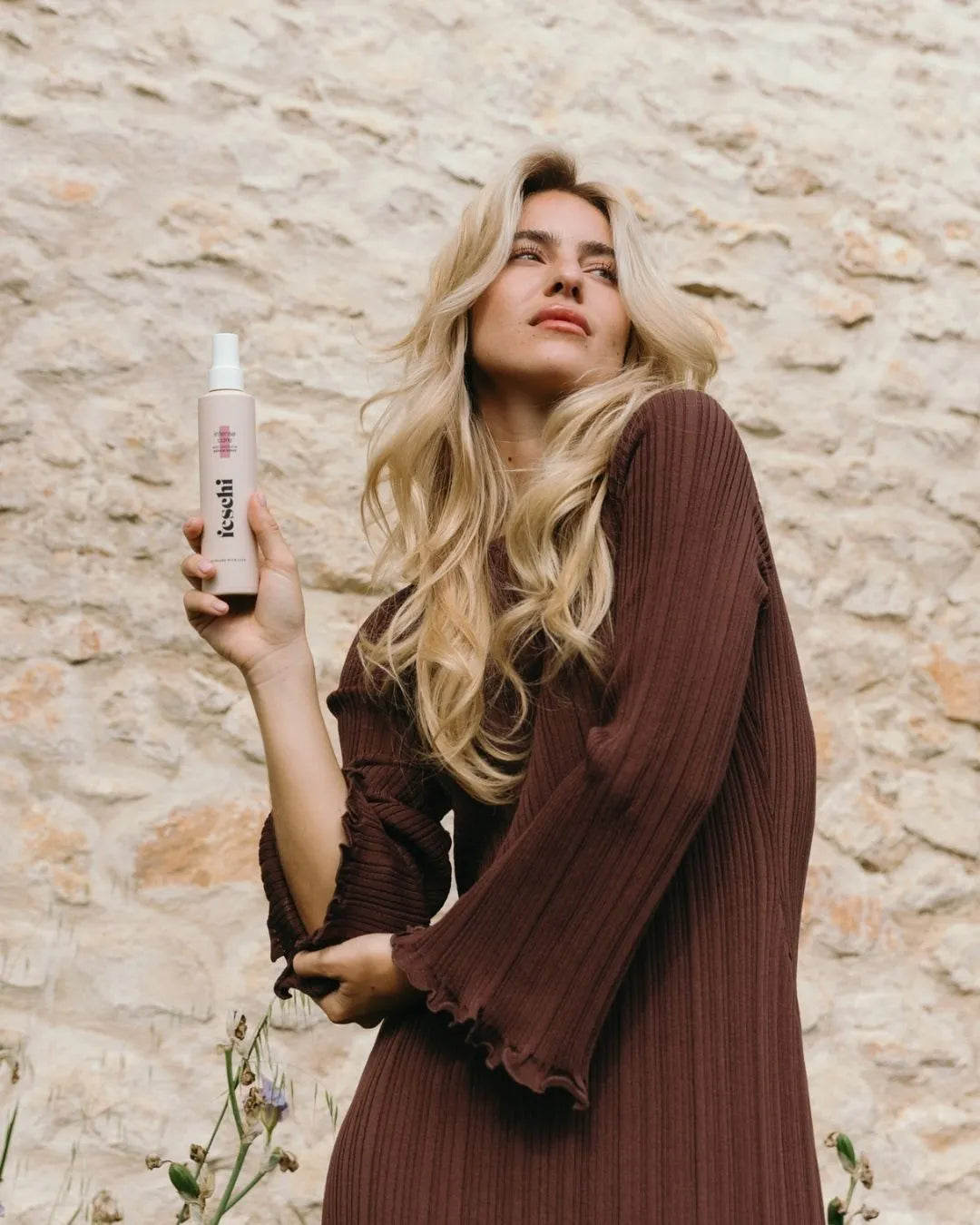 Frau steht vor einer Hauswand und hält das feschi Intense Care Repair Spray in der Hand