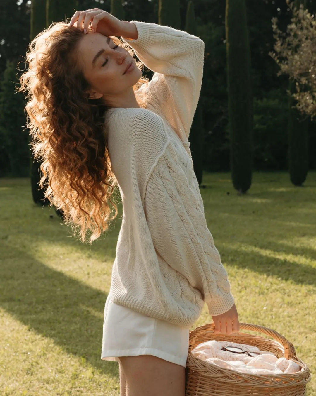 Frau mit Locken steht auf der Wiese und trägt einen Korb