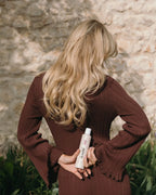 Frau von hinten mit langen blonden Haaren hält hinter dem Rücken das feschi Intense Care Shampoo