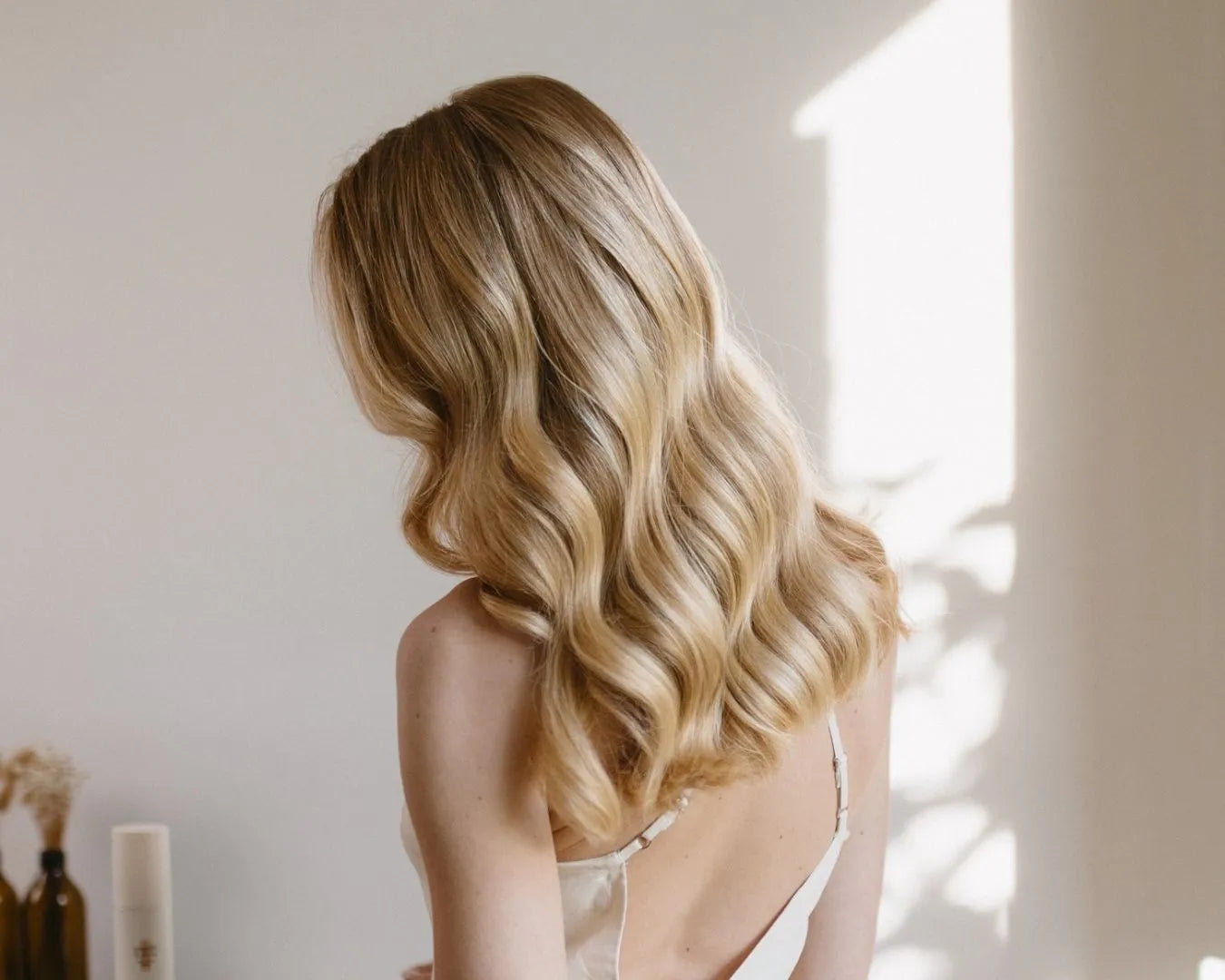 Frau mit langen blonden, welligen Haaren von hinten, im Hintergrund der feschi Smooth & Shine Anti-Frizz Spray