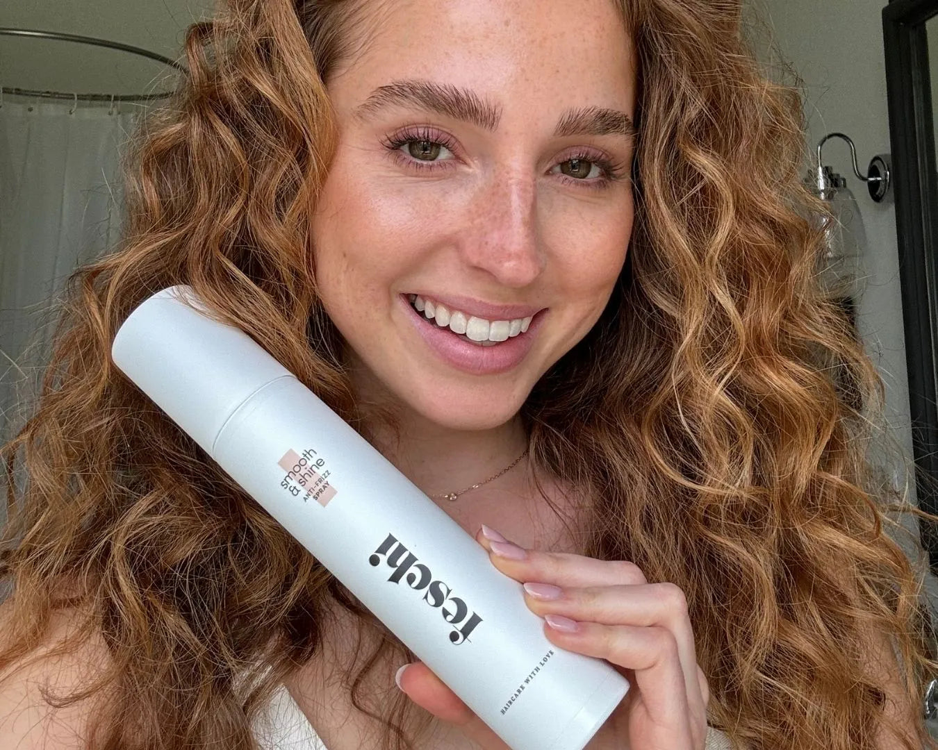 Frau mit lockigen Haaren hält Anti Frizz Spray von feschi in der Hand