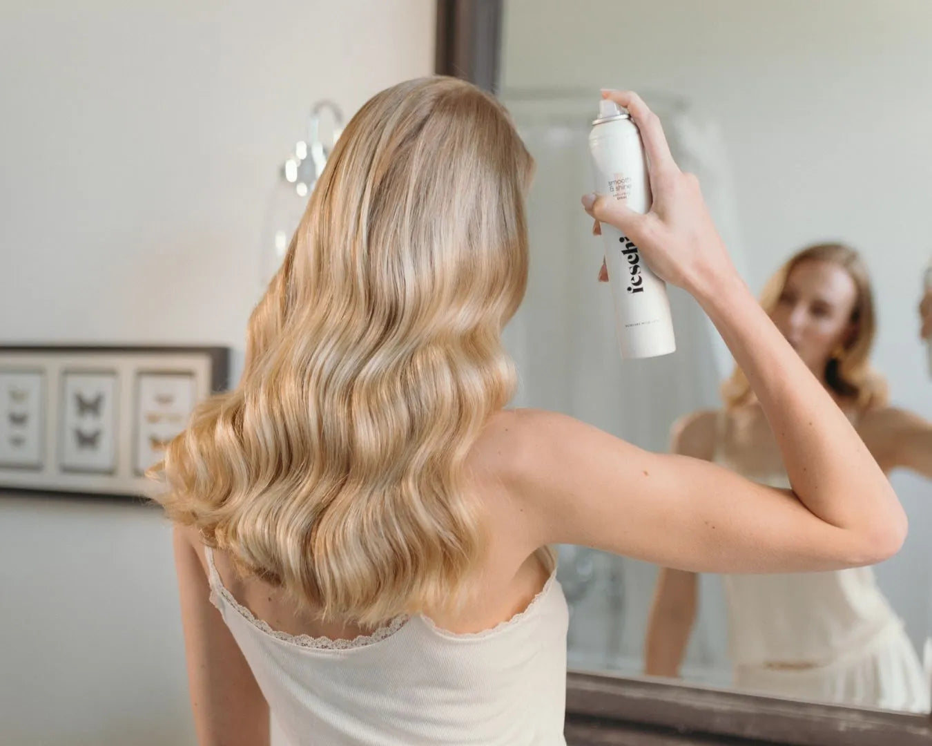 Frau mit langen blonden Haaren von hinten sprüht sich das feschi Smooth & Shine Anti-Frizz Spray von feschi auf die Haare