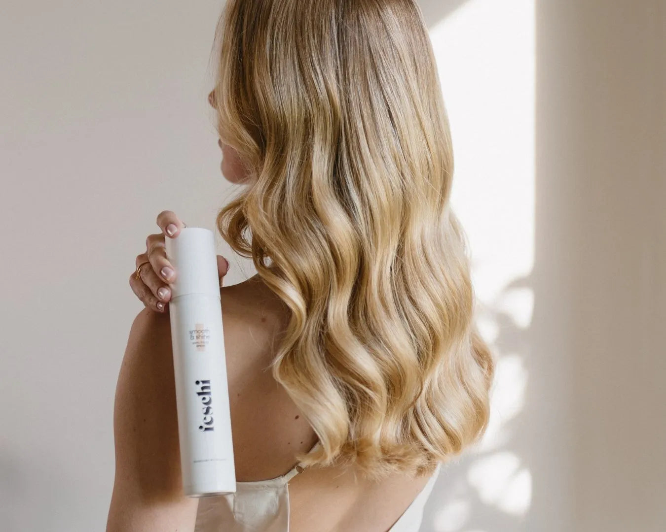Frau mit langen blonden Haaren von hinten hält über ihre Schulter das feschi Smooth & Shine Anti-Frizz Spray