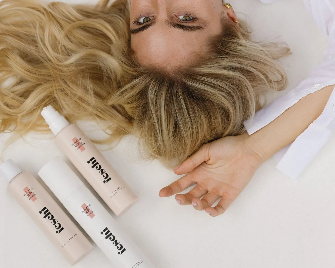 Blonde Frau liegt auf weißem Untergrund und drei feschi Produkte sind über ihr hingelegt