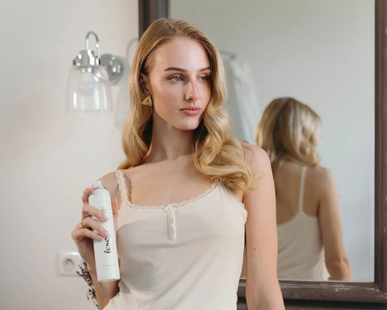 Frau steht vor Spiegel und hält das Anti Frizz Spray von feschi in der Hand