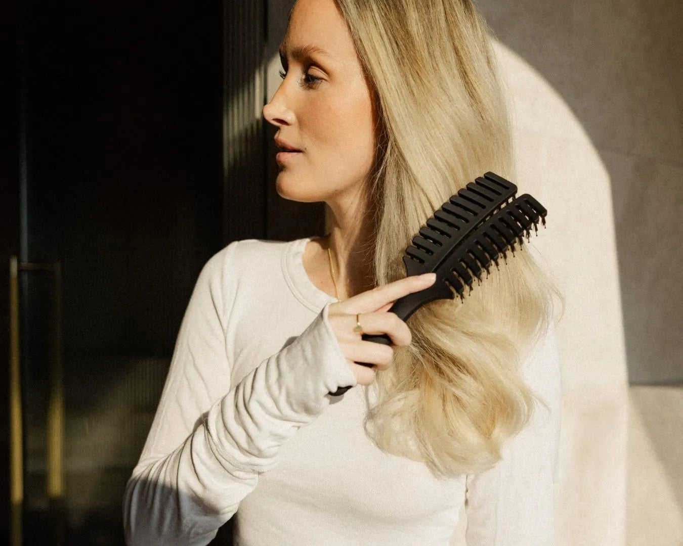 Frau mit blonden, langen Haaren bürstet sich die trockenen Haare mit der feschi Hair Brush