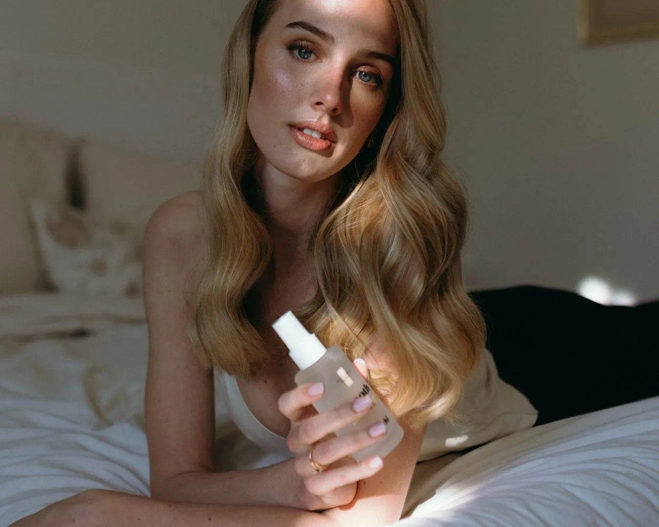 Frau liegt auf dem Bauch im Bett und hält das smooth & shine - Macadamia Haaröl von feschi in der Hand
