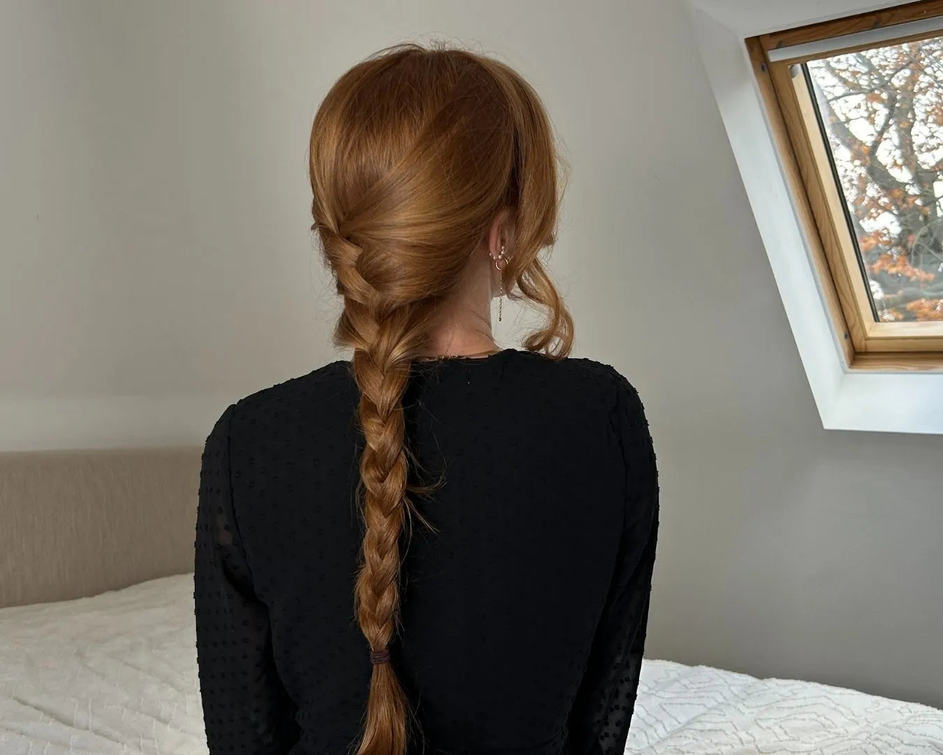 Frau von hinten, sitzend auf dem Bett, mit langen roten Haaren zu einem geflochtenen Zopf