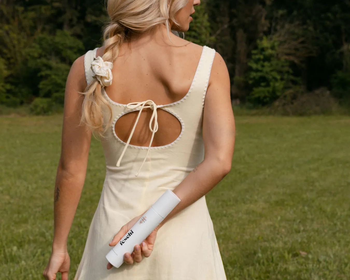 Frau im gelben Kleid ist von hinten zu sehen und hält den anti frizz spray von feschi hinter ihrem rücken