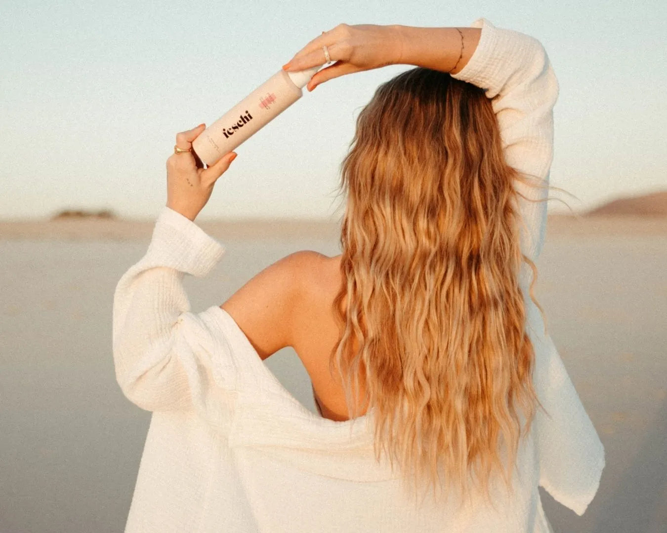 Frau mit langen blonden Haaren von hinten und sie hält ein feschi Haarprodukt schräg über ihren Kopf